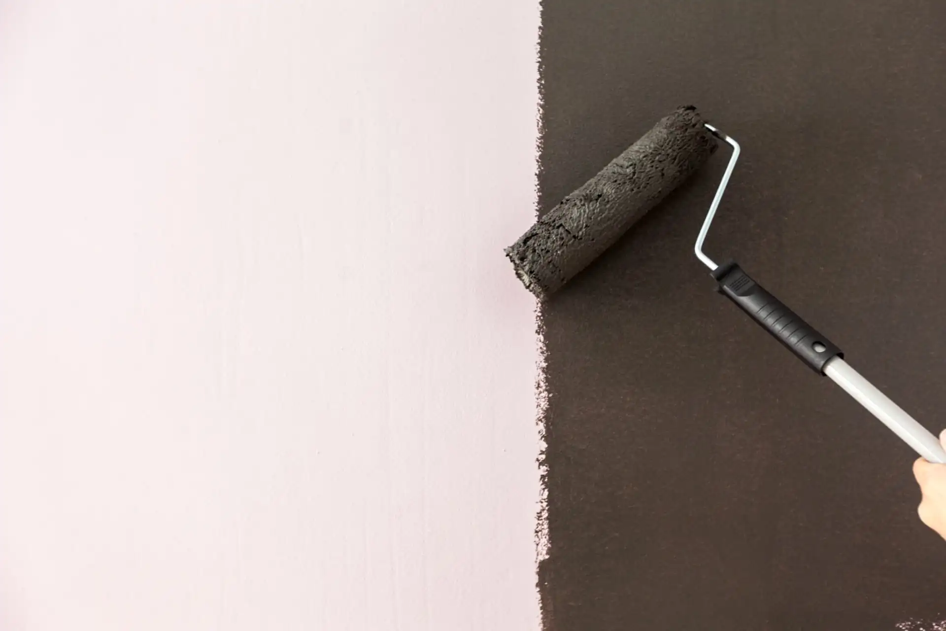 Paint roller applying dark charcoal paint next to a soft pink wall