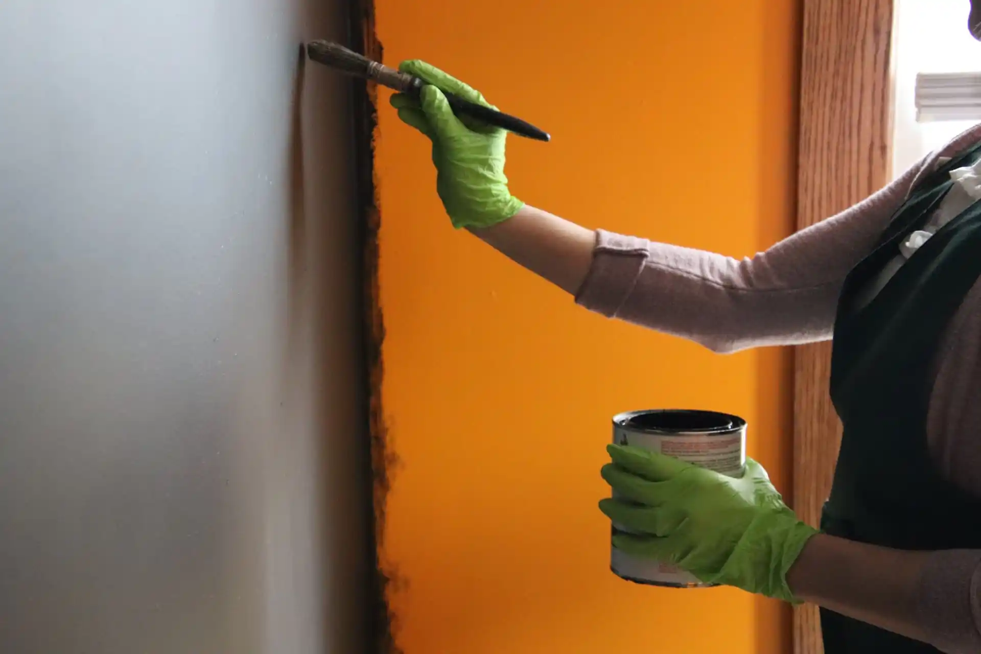 Painter applying orange and charcoal paint to an interior wall